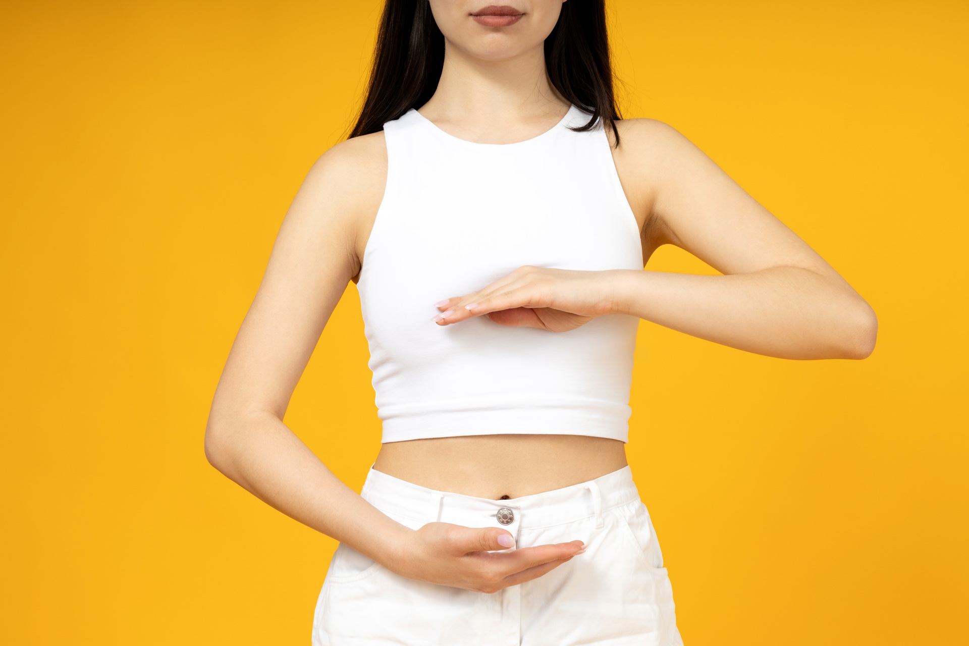 The girl points to her stomach with two hands, on a yellow background.